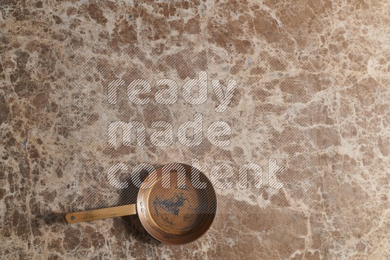 A small copper pan on beige marble background