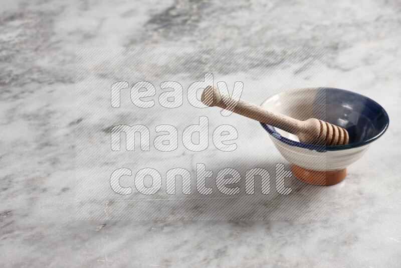 Multicolored pottery bowl with wooden honey dipper in it on grey marble background