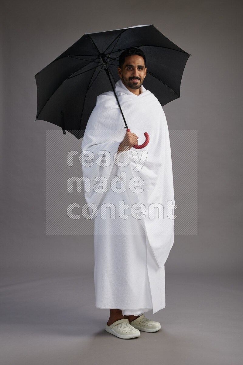 A man wearing Ehram Standing holding umbrella on gray background