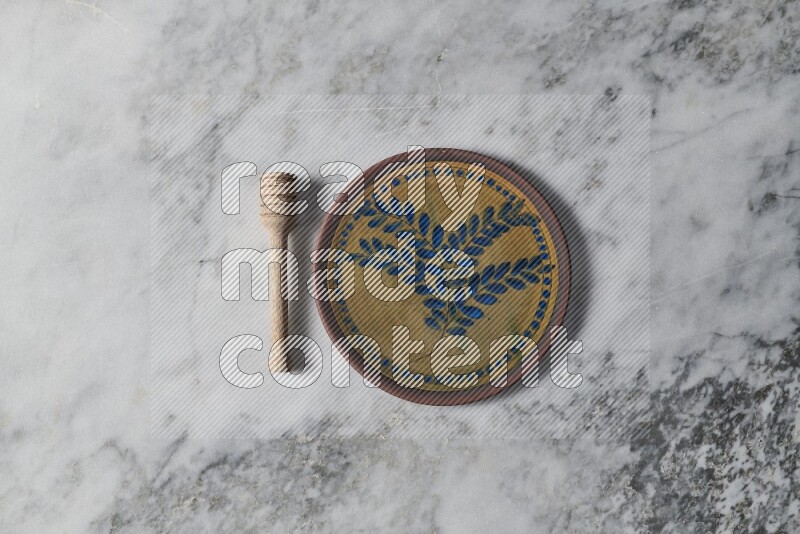 Decorative pottery plate with wooden honey dipper on the side on grey marble background