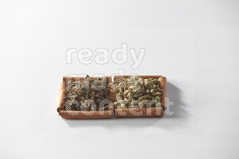 مربعان من أعواد القرفة ممتلئان بحبوب الهيل والريحان المجفف علي خلفية بيضاء