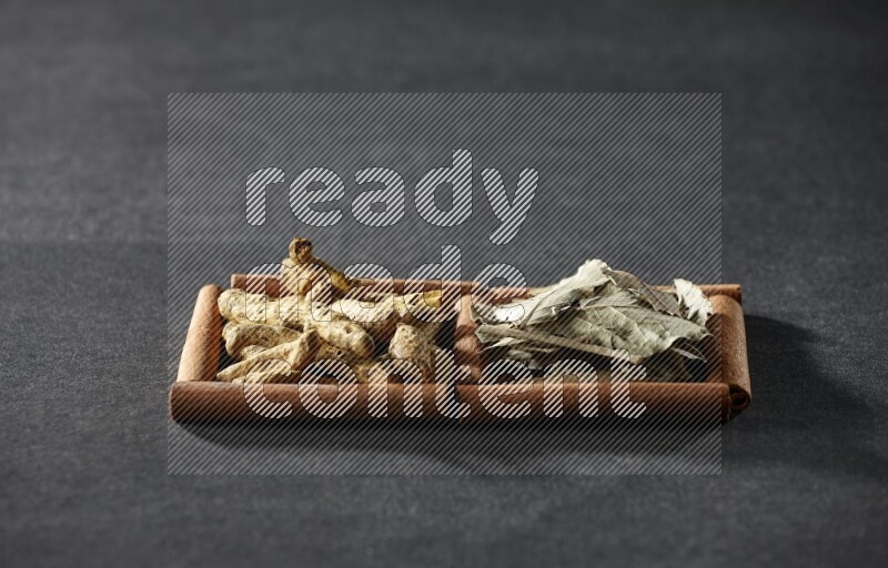 مربعان من أعواد القرفة ممتلئان بأوراق الغار وأصابع الكركم علي خلفية سوداء