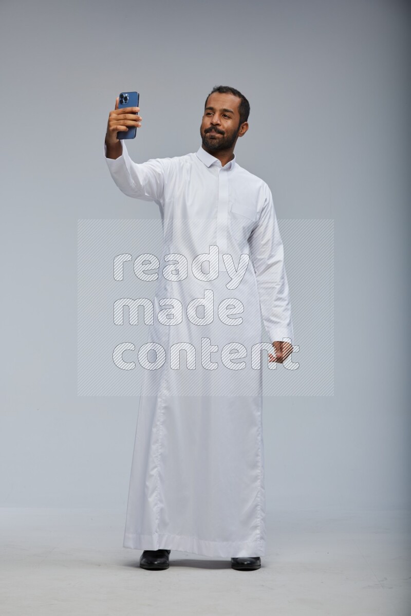 Saudi man wearing Thob standing taking selfie on Gray background