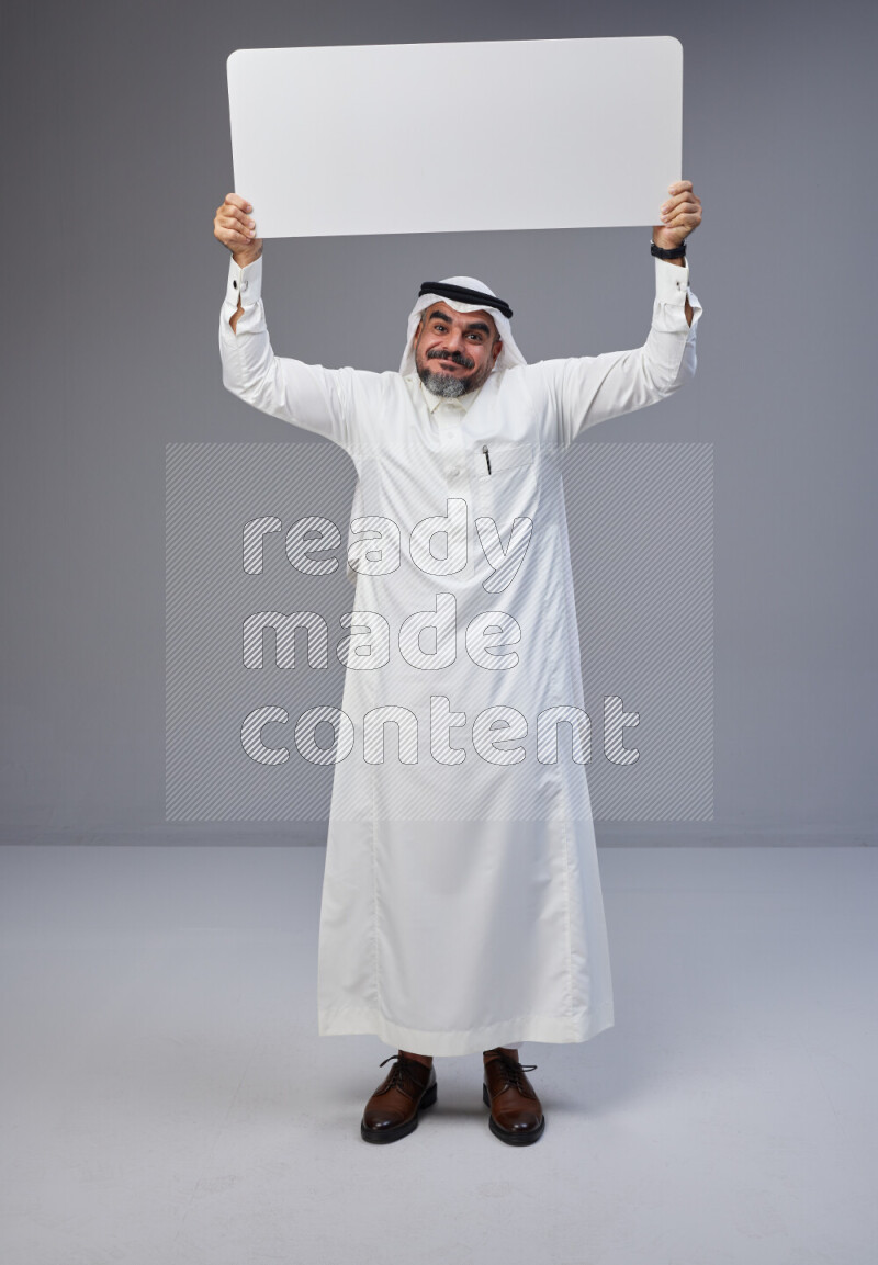 Saudi man Wearing Thob and white Shomag standing holding board on Gray background