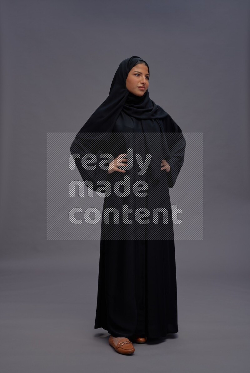 Saudi woman wearing Abaya standing interacting with the camera on gray background
