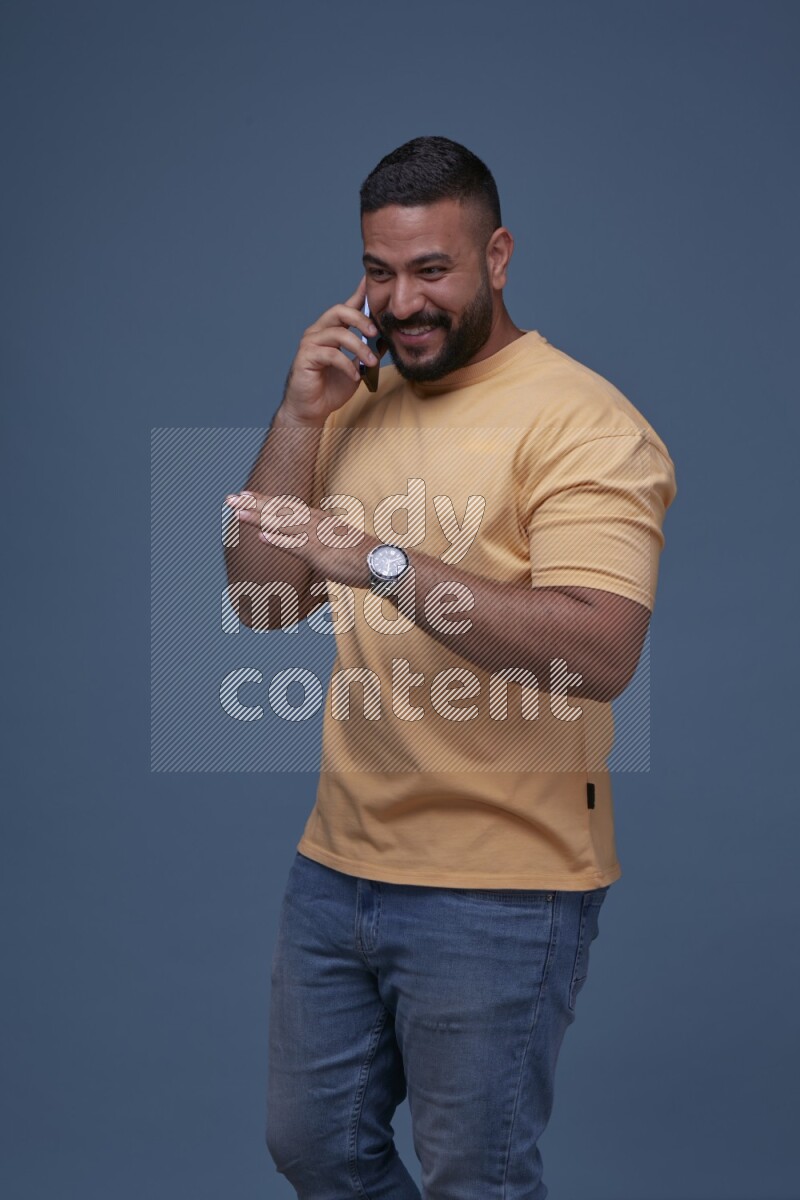 رجل يرتدي بنطال ازرق جينز وقميص اصفر بأكمام قصيره يتحدث بجواله