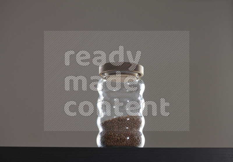 Brown lentils in a glass jar on black background