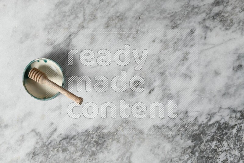 Multicolored pottery bowl with wooden honey dipper in it on grey marble background