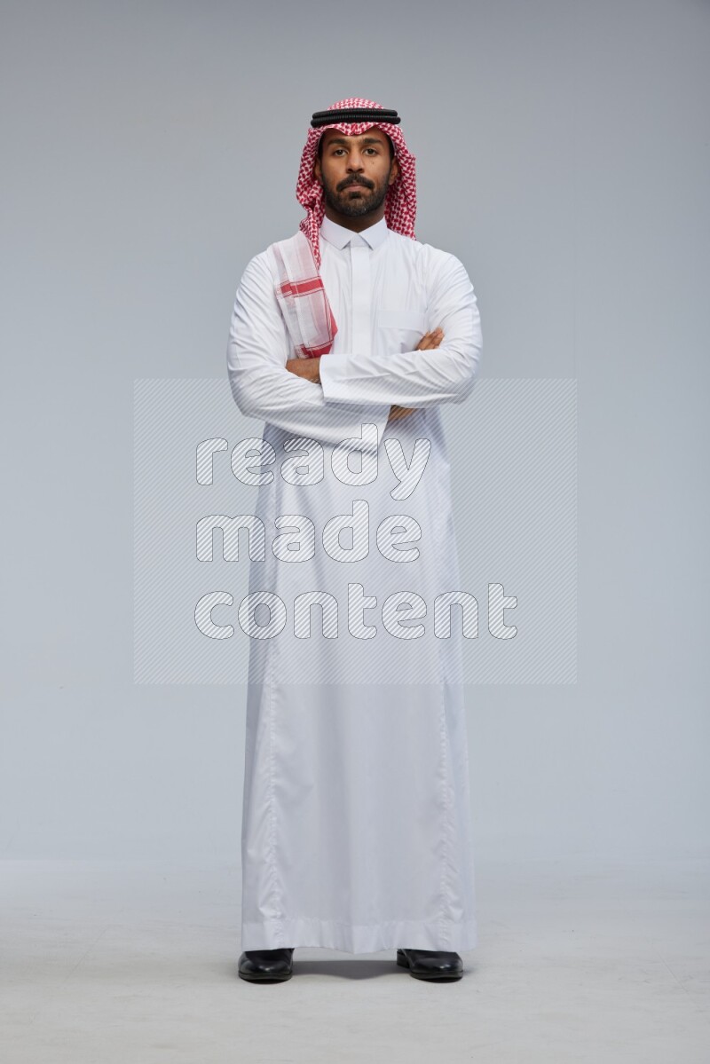 Saudi man Wearing Thob and shomag standing with crossed arms on Gray background