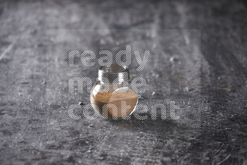 Herbal glass jar full of cinnamon powder on a textured black background