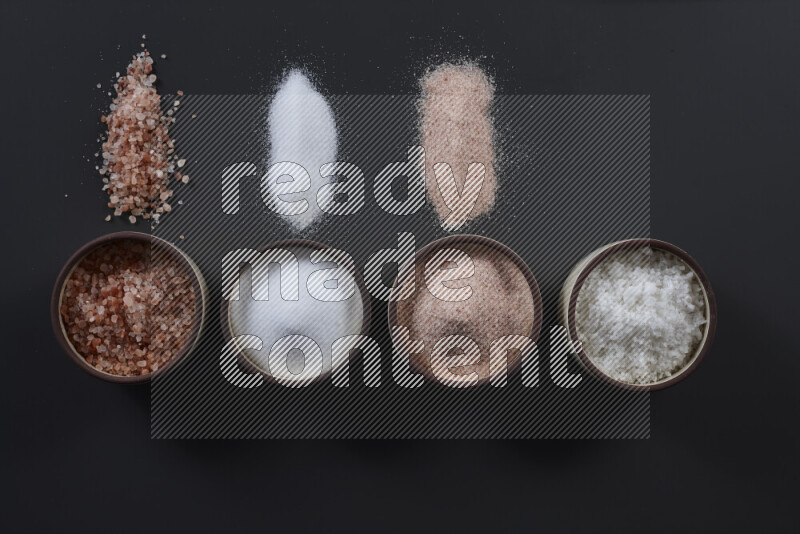 4 pottery bowls filled with himalayan salt and white salt on black background