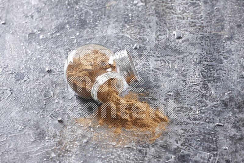 Flipped herbal glass jar full of cinnamon powder on textured black background