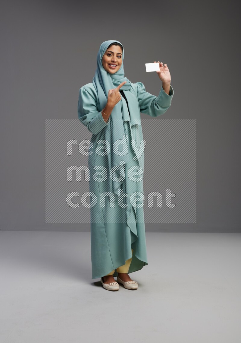 Saudi Woman wearing Abaya standing holding ATM card on Gray background