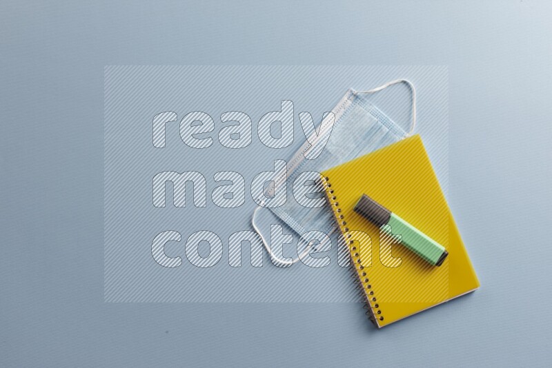 A yellow notebook with different school supplies on blue background