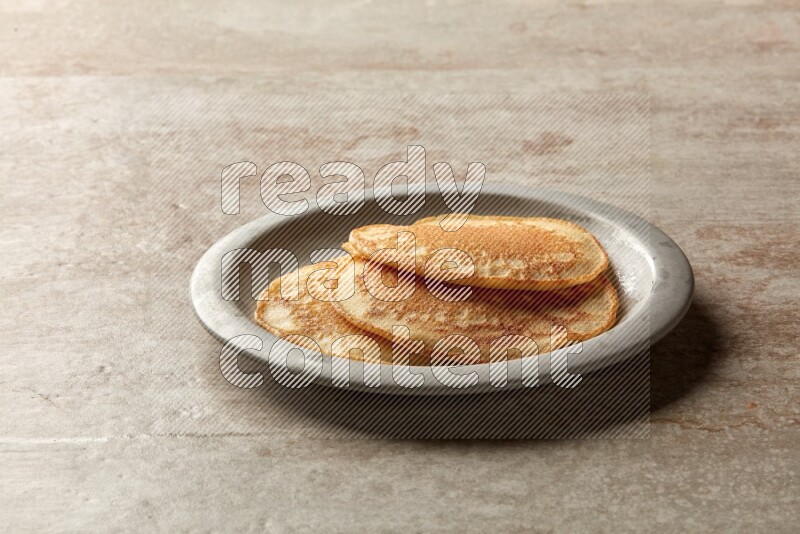 Three stacked plain pancakes in a grey plate on beige background
