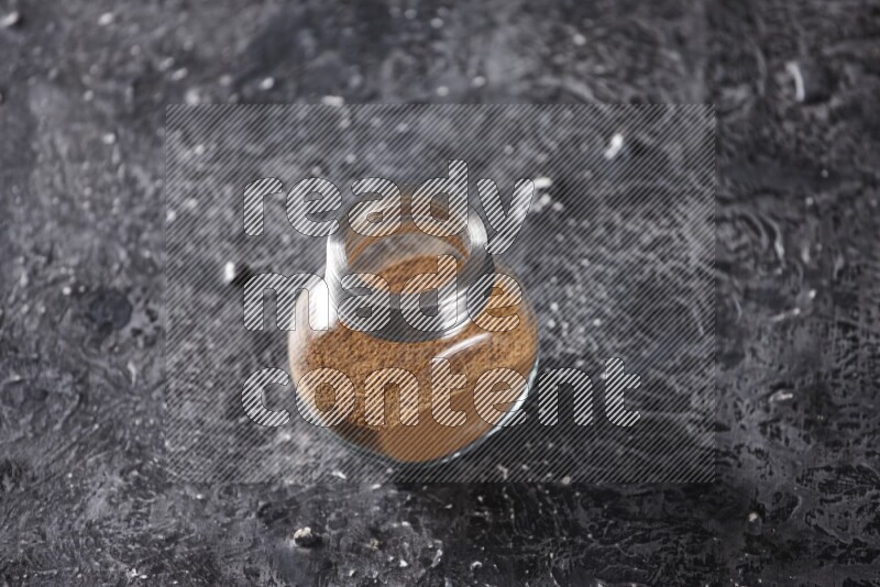 Herbal glass jar full of cinnamon powder on a textured black background