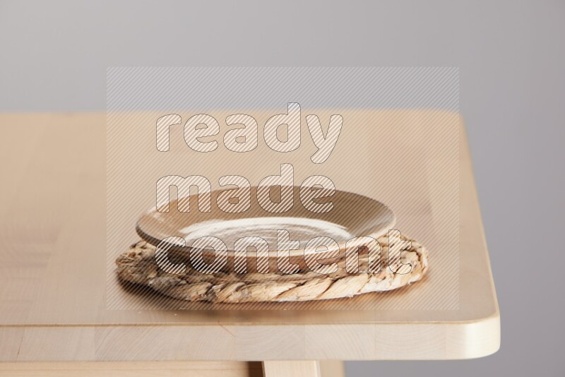 multi-colored pottery Plate placed on a small light colored straw placemat on the edge of wooden table