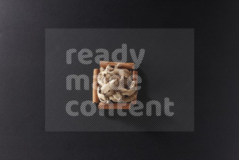A single square of cinnamon sticks full of dried ginger on black flooring