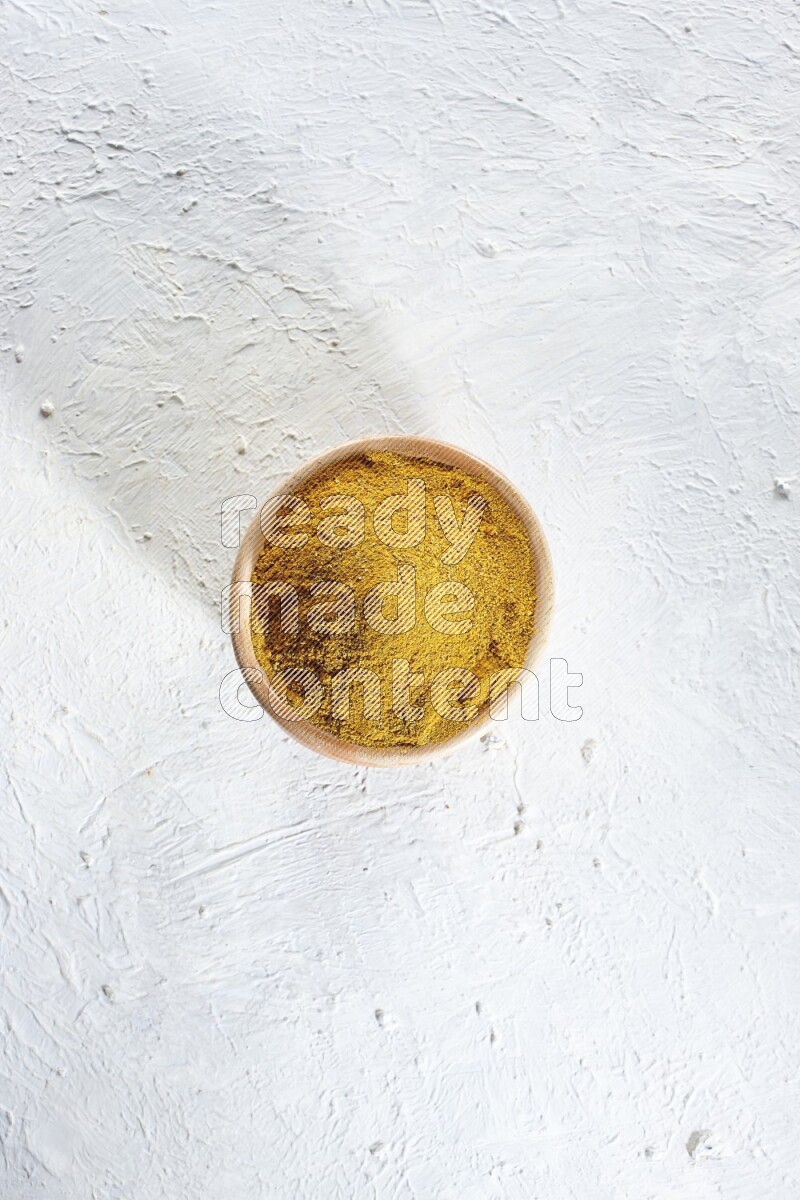 A wooden bowl full of turmeric powder on a textured white flooring