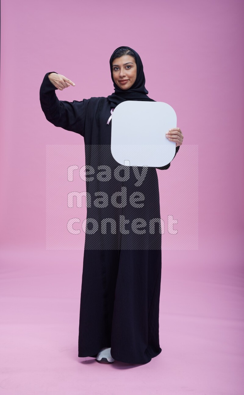 Saudi woman wearing pink ribbon on Abaya standing holding social media signs on pink background