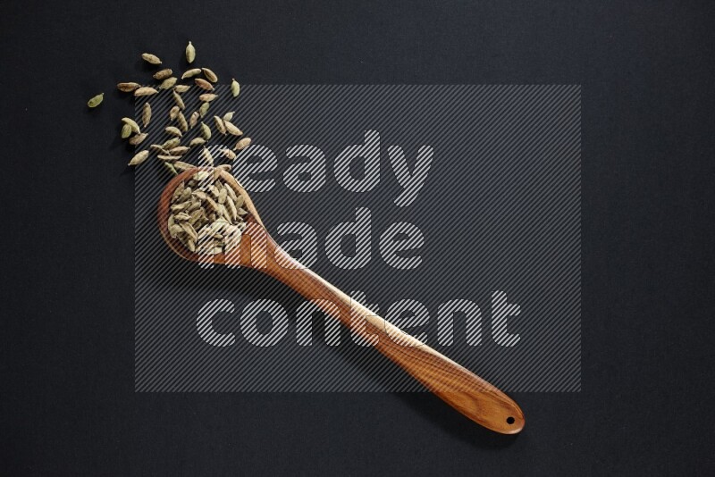 A wooden ladle full of cardamom on black flooring