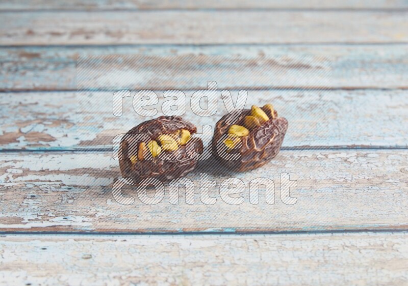 two pistachio stuffed madjoul dates on a light blue wooden background