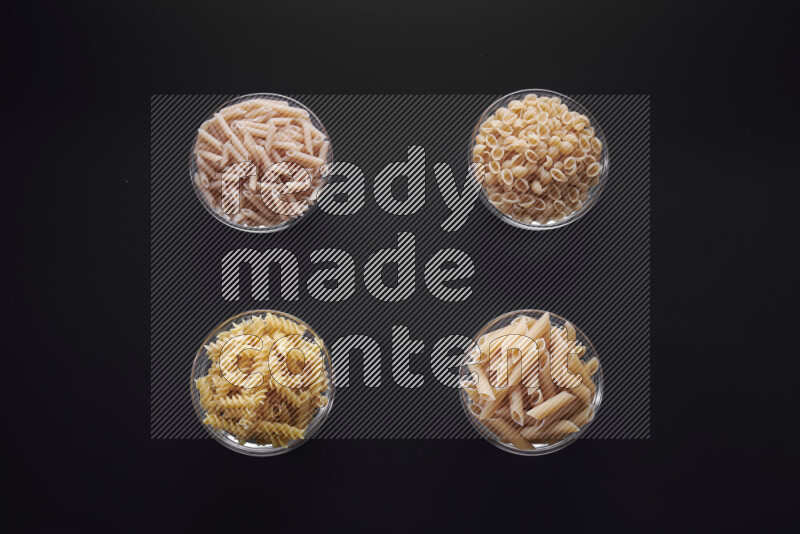 Different pasta types in glass bowls on black background