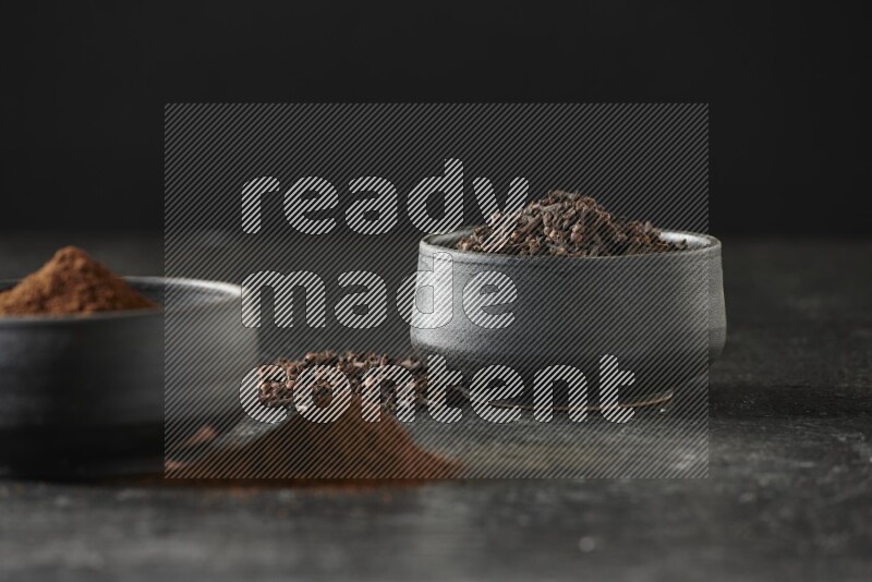 وعاءين من الفخار الأسود أحدهما ممتلئي بحبوب القرنفل والآخر ممتلئ ببودرة القرنفل على خلفية سوداء