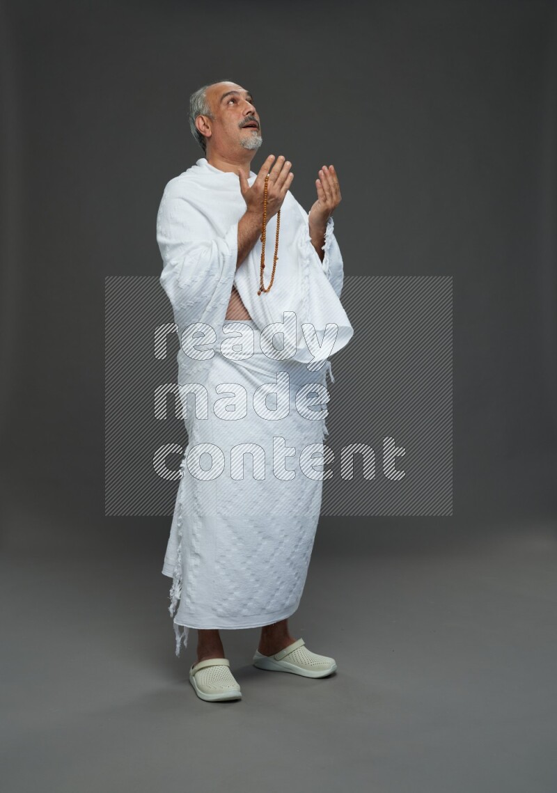 A man wearing Ehram Standing dua'a on gray background