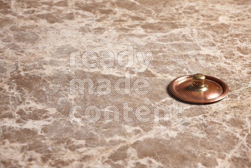 A small copper pot lid on beige marble background