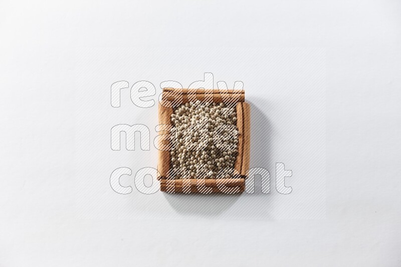 A single square of cinnamon sticks full of white pepper on white flooring