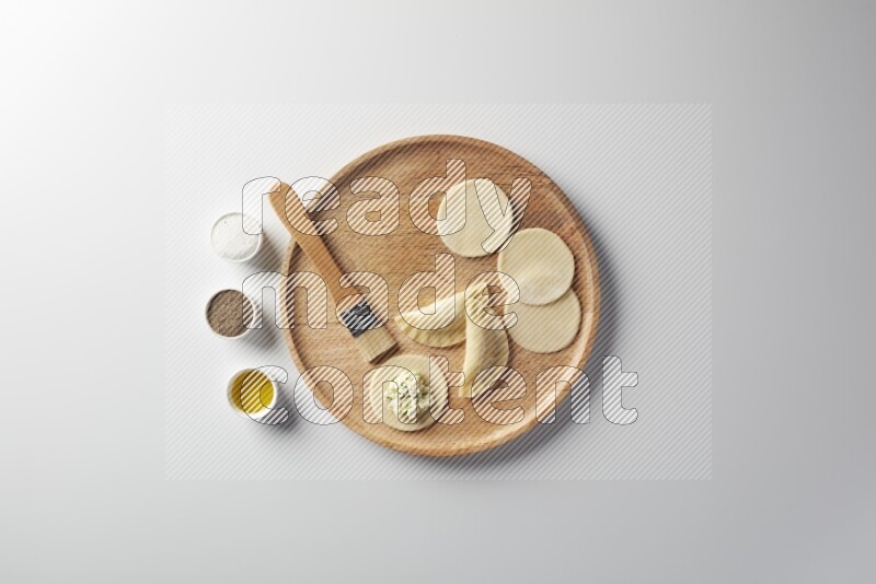 two closed sambosas and one open sambosa filled with cheese while salt, black pepper and oil with oil brush aside in a wooden dish on a white background