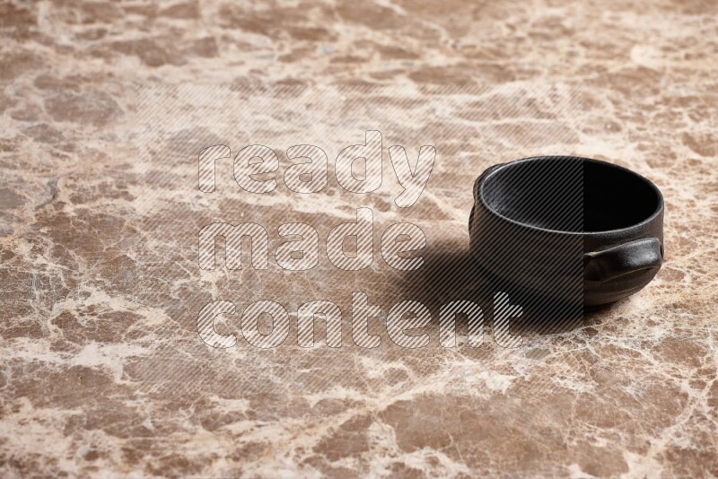 A black pottery bowl on beige marble background