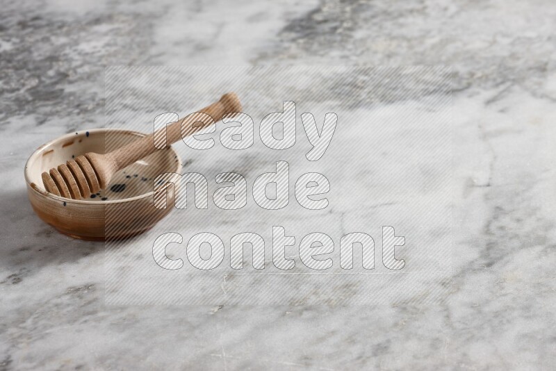 Multicolored pottery bowl with wooden honey dipper in it on grey marble background