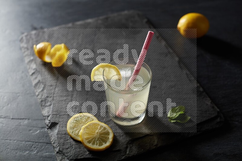 A glass of lemon juice with a straw on black background