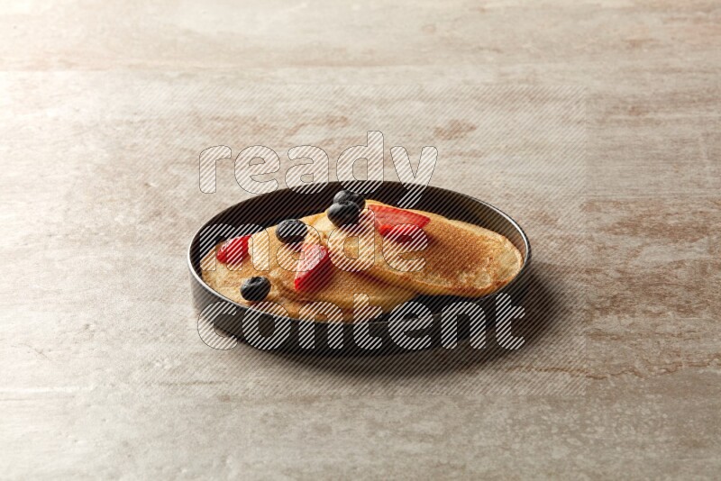 Three stacked mixed berries pancakes in a black plate on beige background