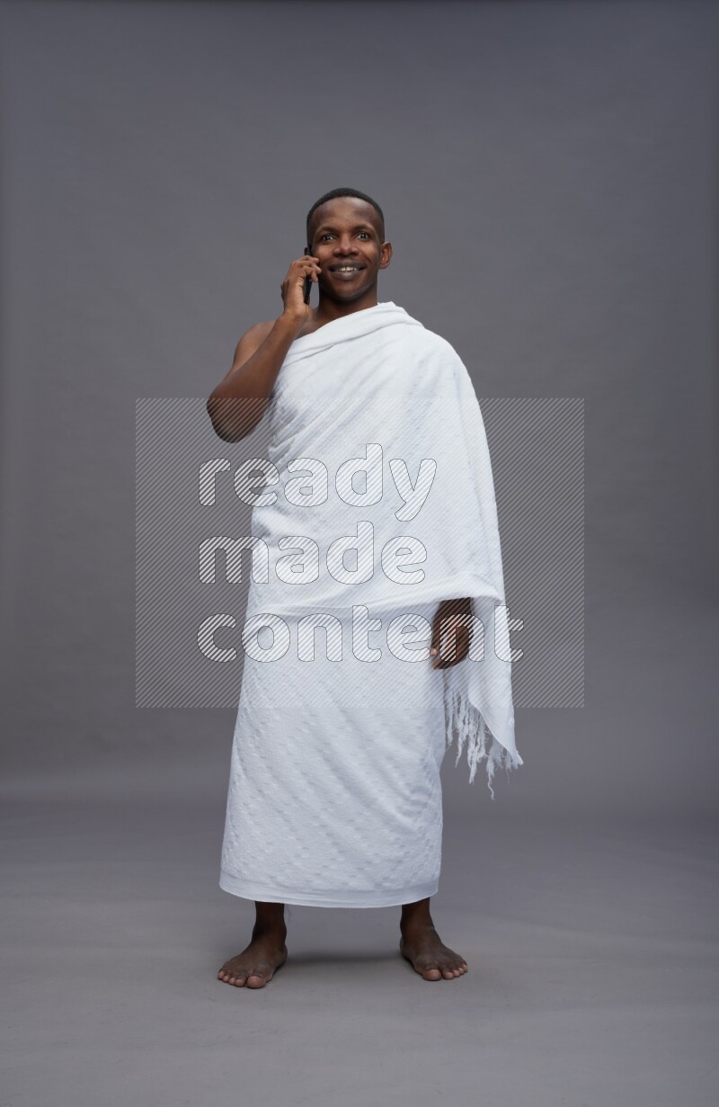 A man wearing Ehram Standing talking on phone on gray background