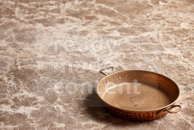 A small copper pan on beige marble background