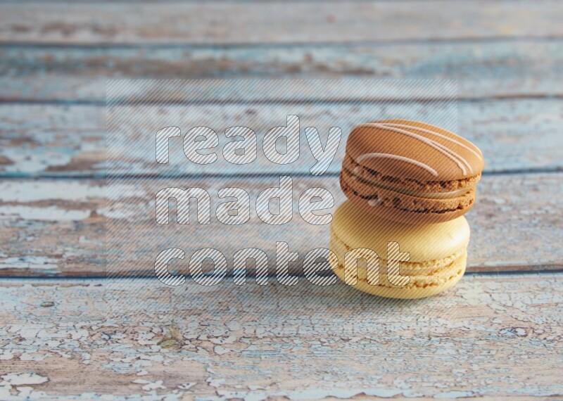 45º Shot of of two assorted Brown Irish Cream, and Yellow Vanilla macarons on light blue background