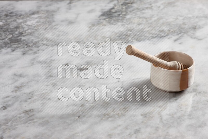 Multicolored pottery bowl with wooden honey dipper in it on grey marble background