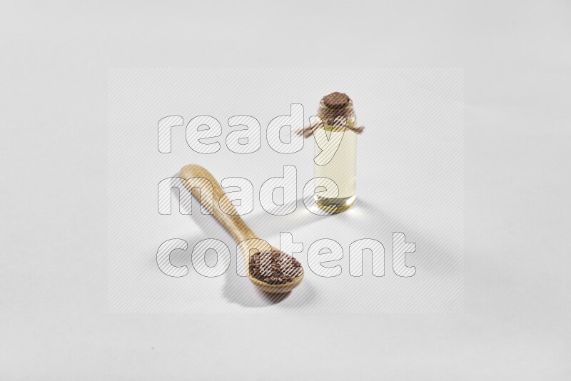 A wooden spoon full of flax seeds and a glass bottle full of flaxseeds oil on a white flooring