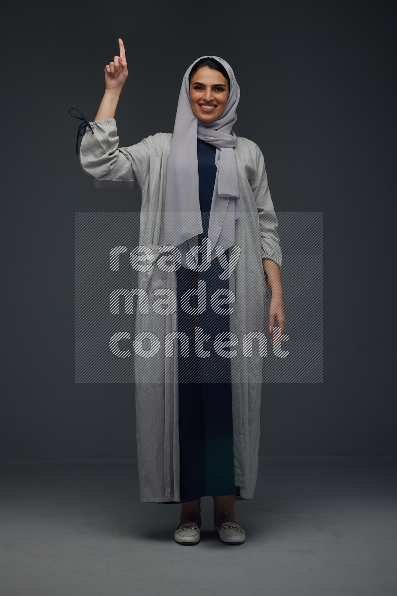 A Saudi woman wearing a light gray Abaya and head scarf standing and making multi poses eye level on a grey background