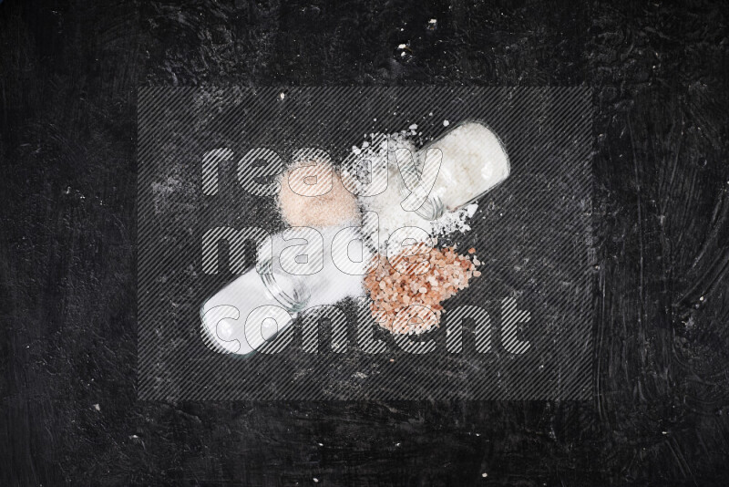 4 glass jars filled with table salt, coarse sea salt, fine himalayan salt and coarse himalayan salt on black background