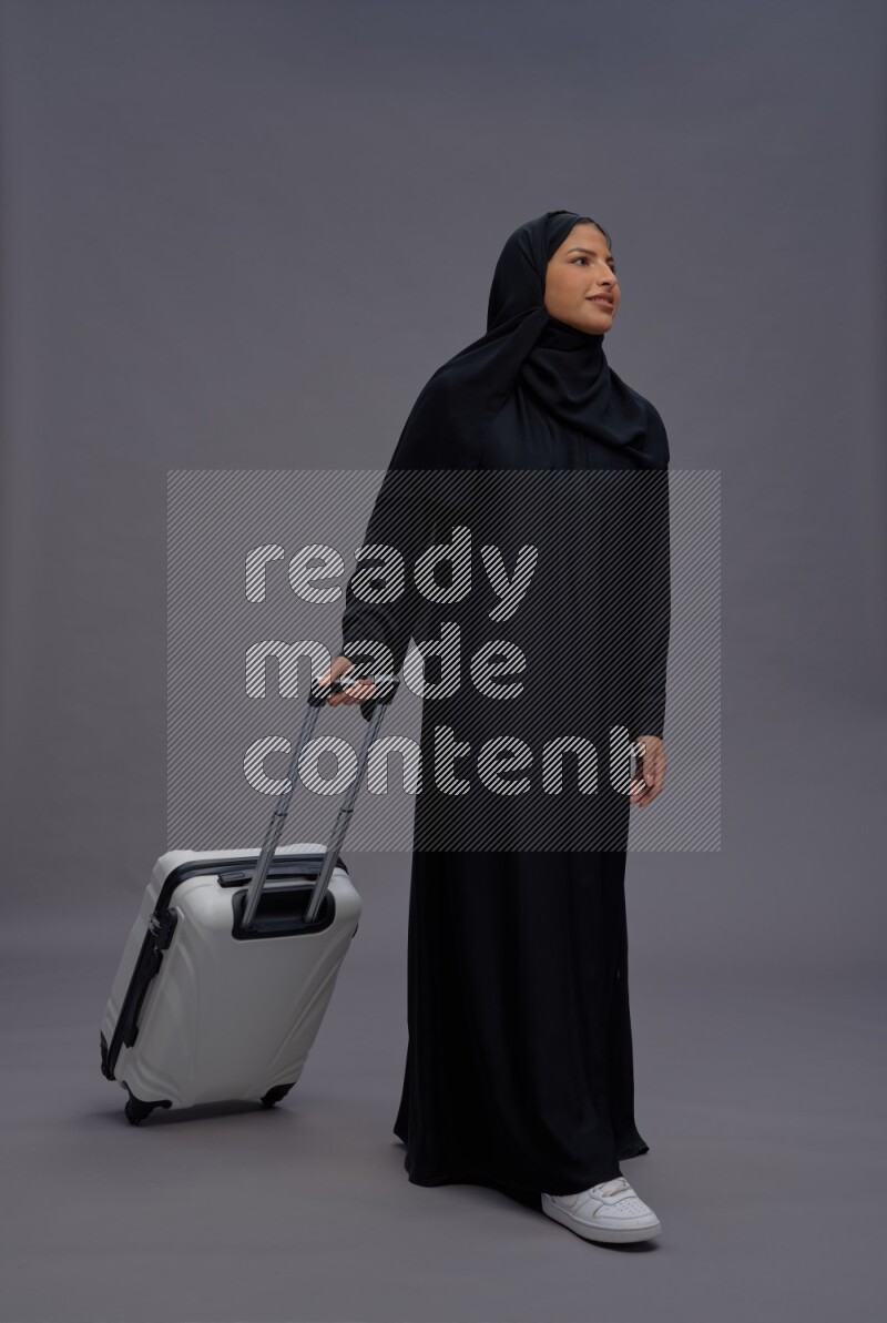 Saudi woman wearing Abaya standing holding bag on gray background