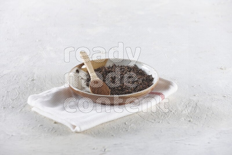 A Pottery plate full of whole cloves and a wooden spoon full of cloves powder in it on a textured white background