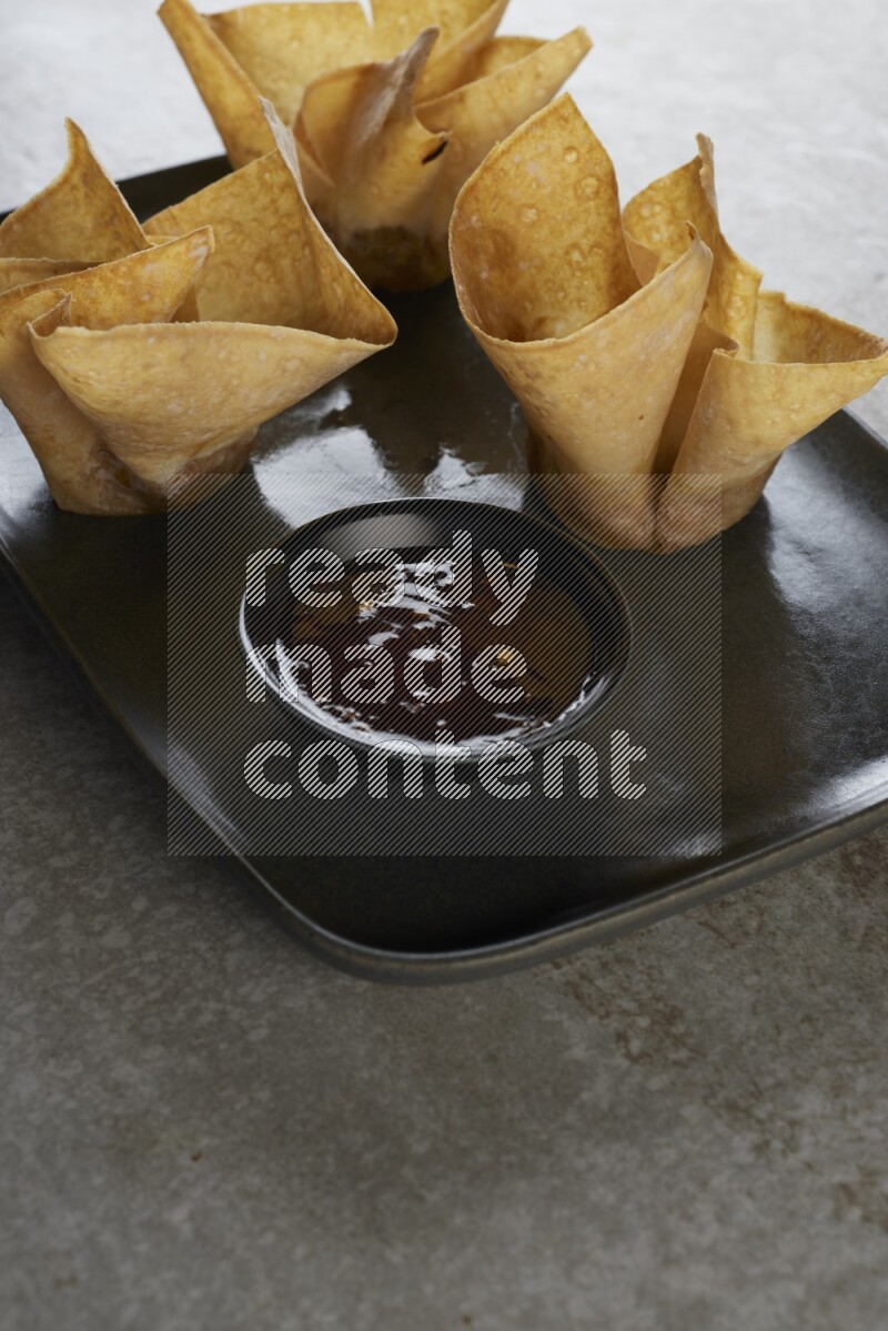 wonton cups with soy sauce ramkin on rectangle dark grey ceramic plate on grey textured counter top