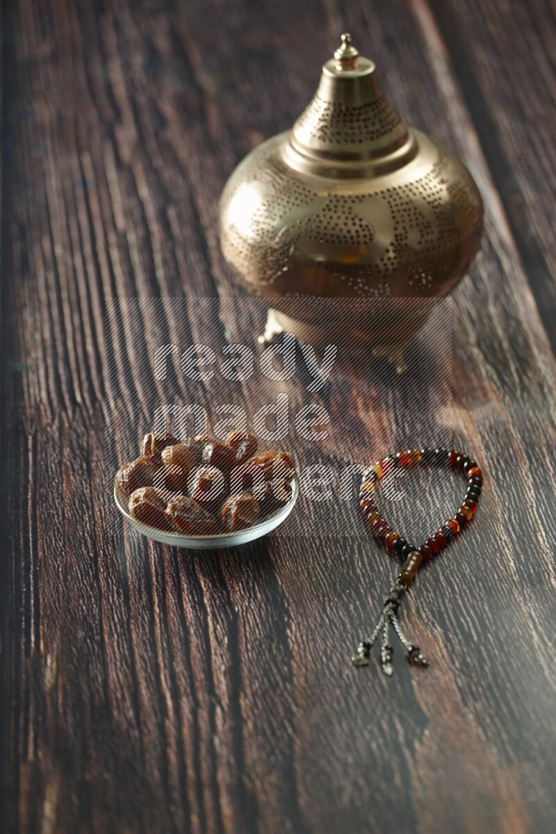 A golden lantern with different drinks, dates, nuts, prayer beads and quran on brown wooden background