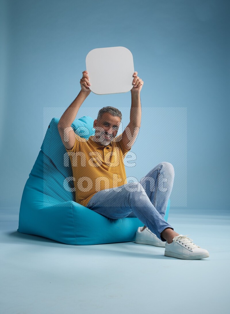 A man sitting on a blue beanbag and holding social media sign