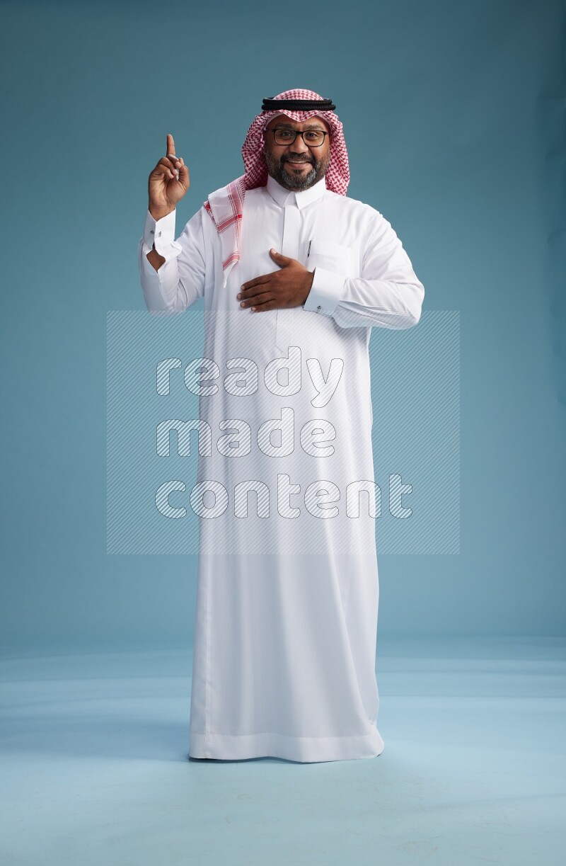 Saudi Man with shimag Standing Interacting with the camera on blue background