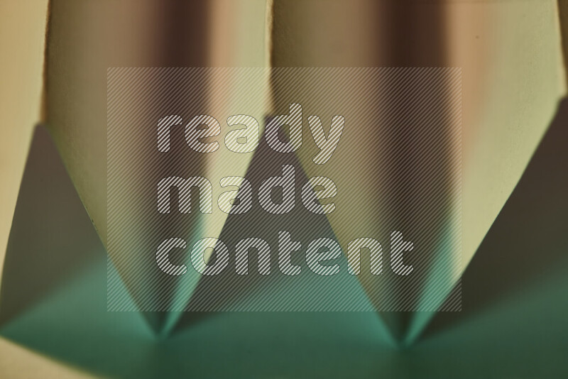 A close-up abstract image showing sharp geometric paper folds in green gradients and warm tones